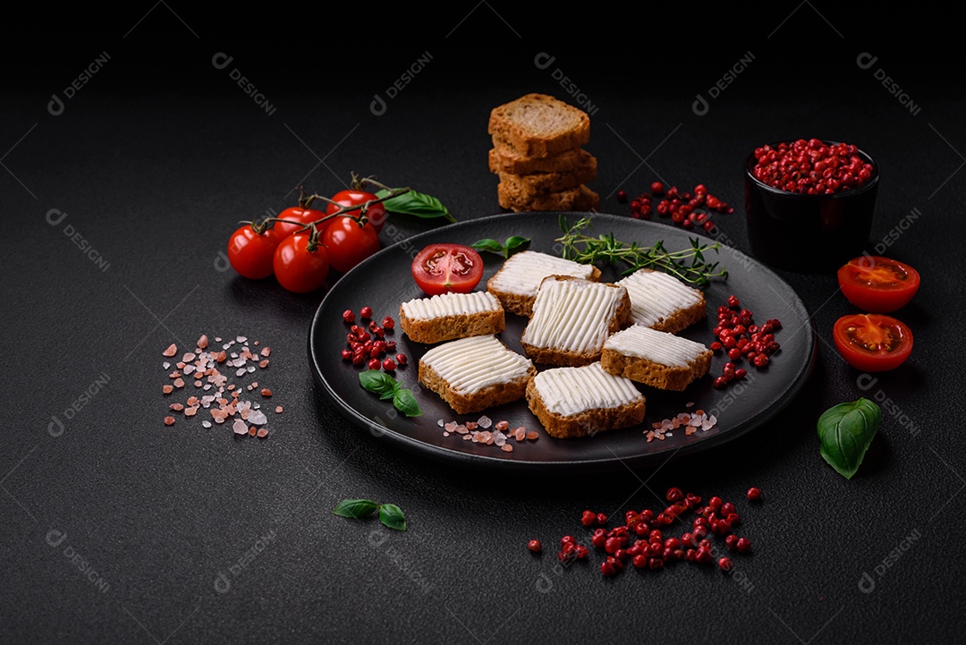 Deliciosos croutons de trigo retangulares salgados com cream cheese, tomate, sal e especiarias sobre um fundo escuro de concreto