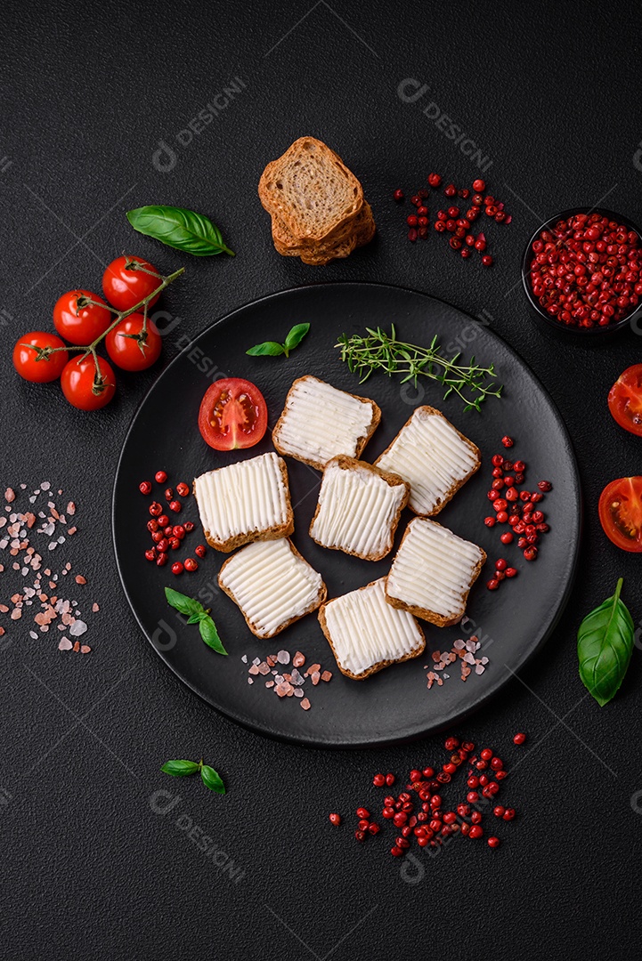 Deliciosos croutons de trigo retangulares salgados com cream cheese, tomate, sal e especiarias sobre um fundo escuro de concreto