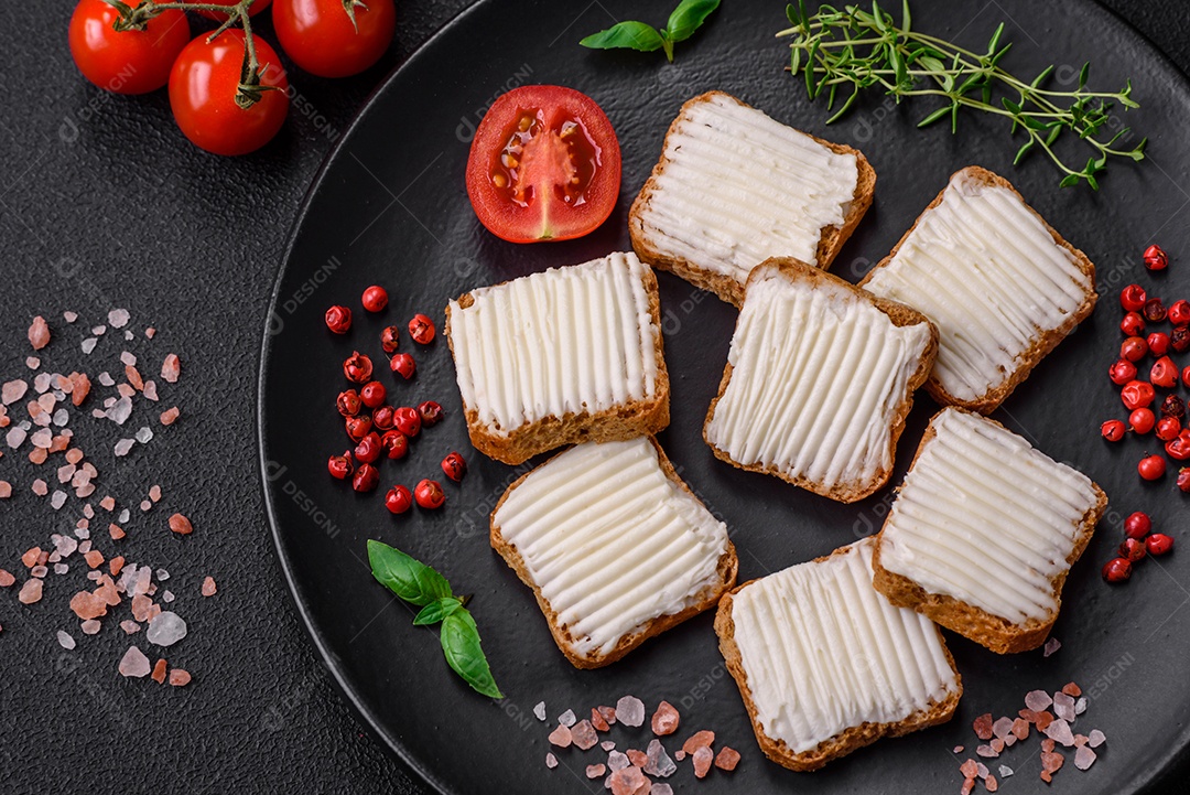 Deliciosos croutons de trigo retangulares salgados com cream cheese, tomate, sal e especiarias sobre um fundo escuro de concreto