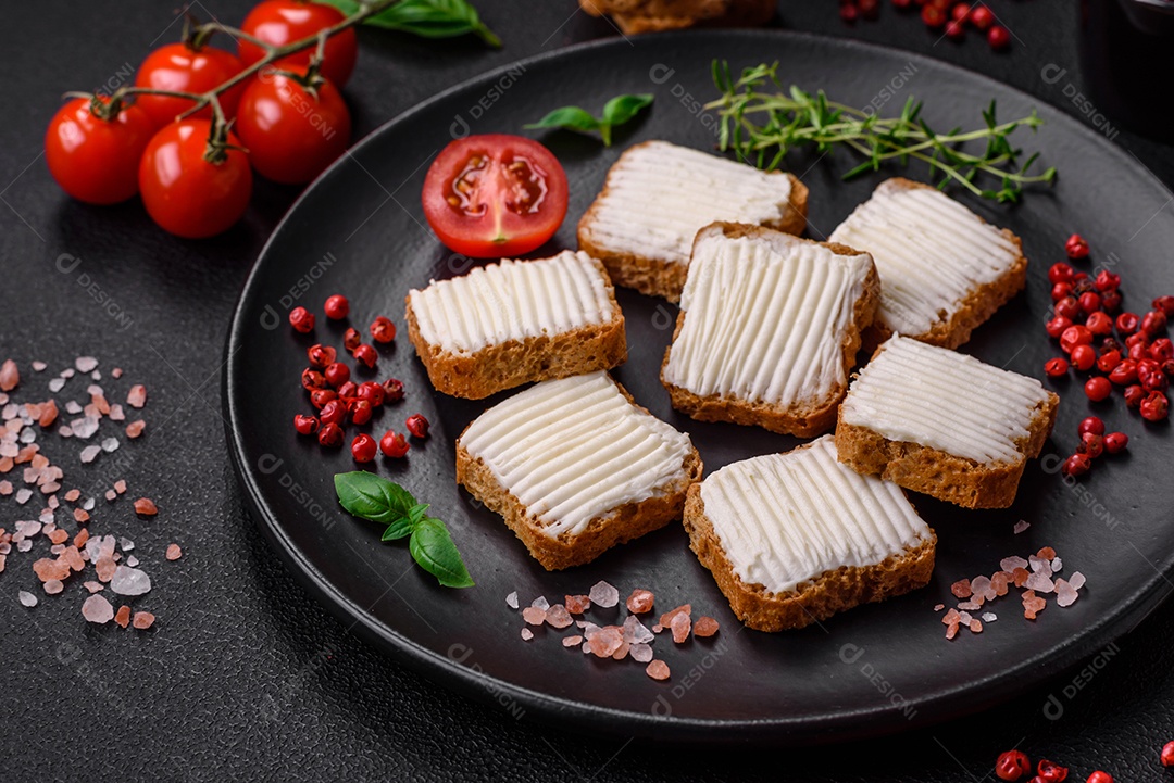 Deliciosos croutons de trigo retangulares salgados com cream cheese, tomate, sal e especiarias sobre um fundo escuro de concreto