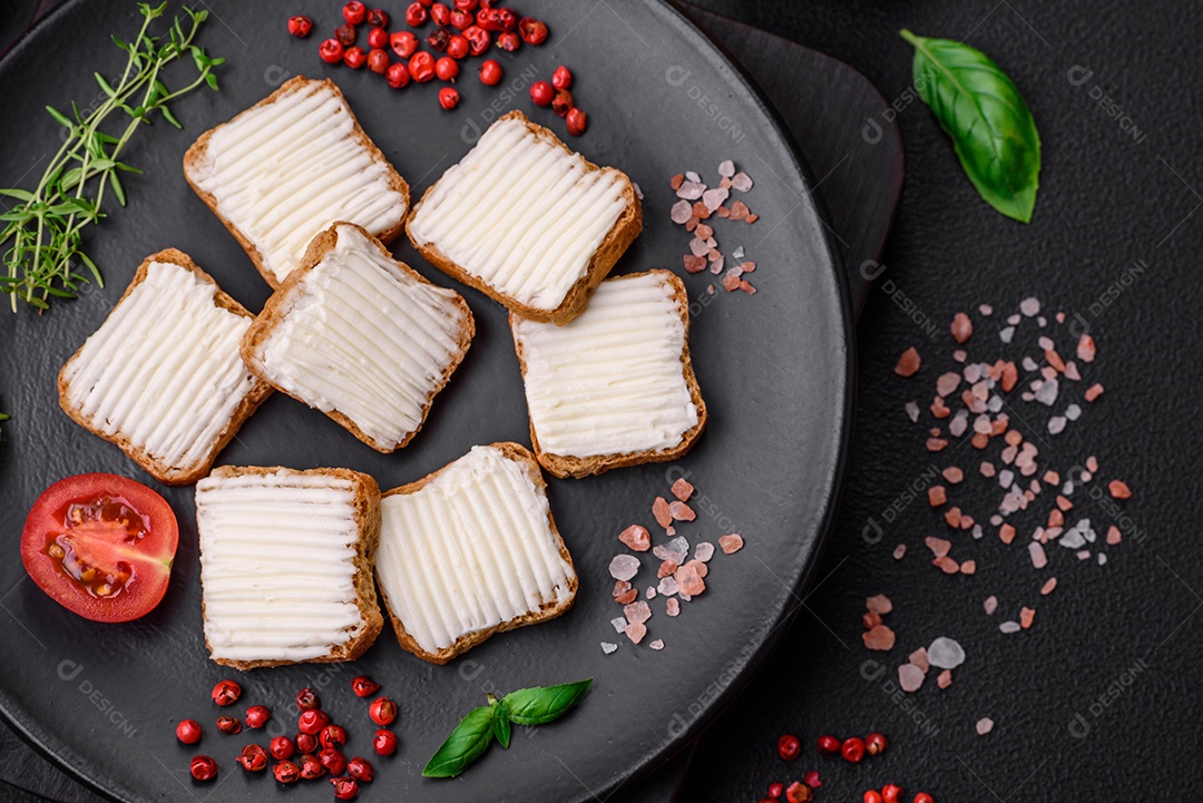 Deliciosos croutons de trigo retangulares salgados com cream cheese, tomate, sal e especiarias sobre um fundo escuro de concreto