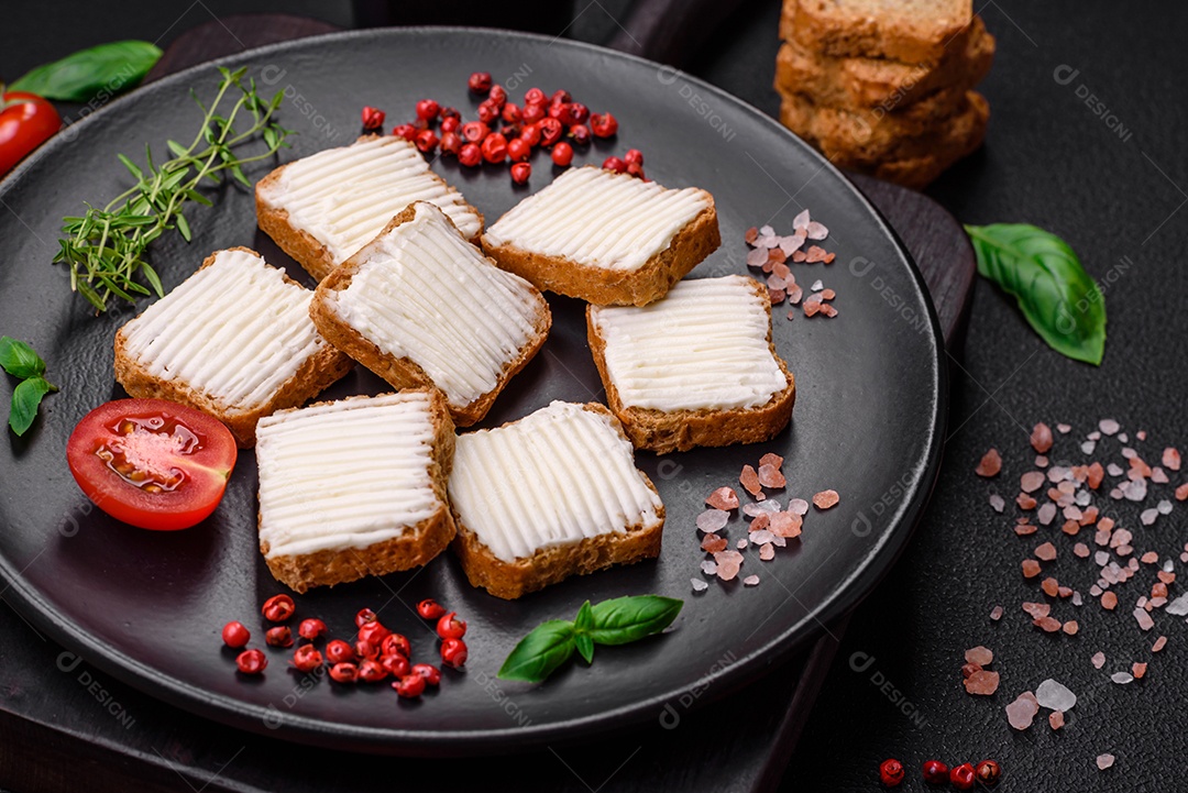 Deliciosos croutons de trigo retangulares salgados com cream cheese, tomate, sal e especiarias sobre um fundo escuro de concreto