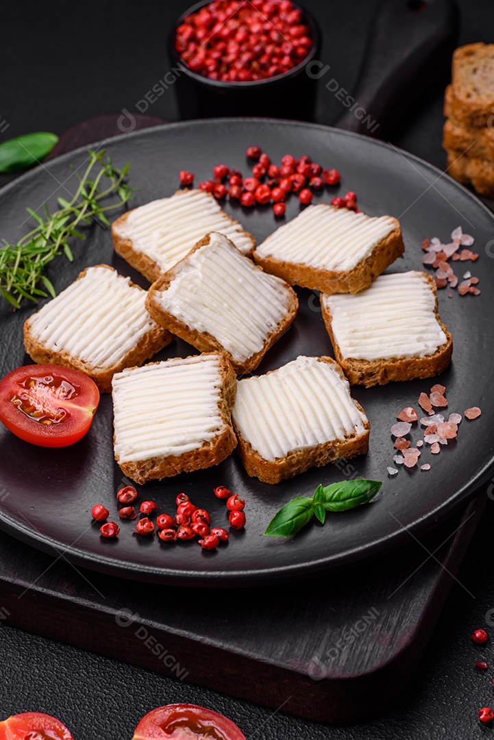 Deliciosos croutons de trigo retangulares salgados com cream cheese, tomate, sal e especiarias sobre um fundo escuro de concreto