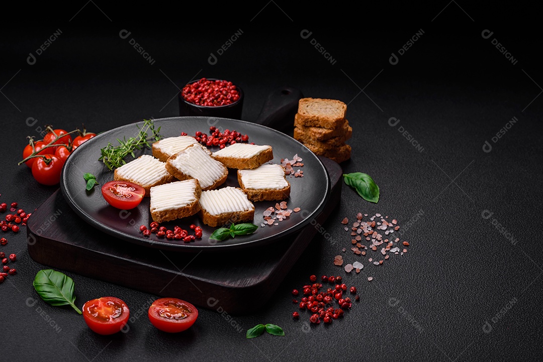 Deliciosos croutons de trigo retangulares salgados com cream cheese, tomate, sal e especiarias sobre um fundo escuro de concreto