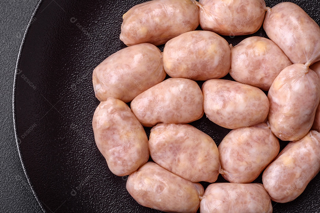 Salsichas cruas frescas de porco ou frango com sal, especiarias e ervas sobre um fundo de concreto texturizado