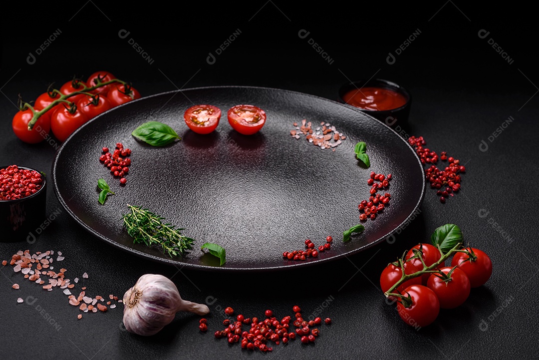 Ingredientes para cozinhar tomate cereja, sal, especiarias e ervas sobre um fundo escuro de concreto