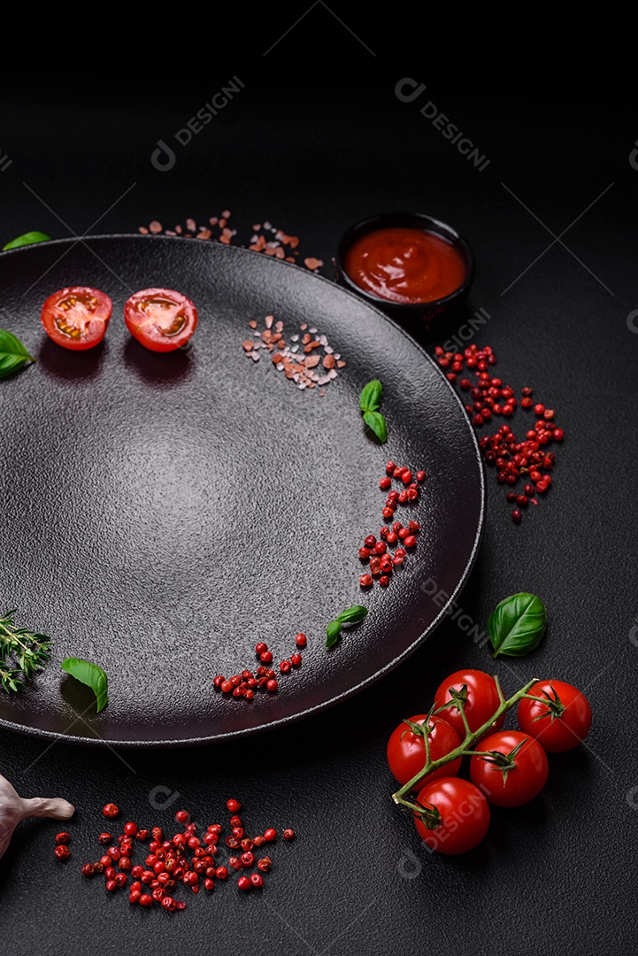 Ingredientes para cozinhar tomate cereja, sal, especiarias e ervas sobre um fundo escuro de concreto