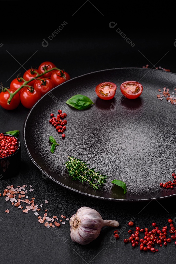 Ingredientes para cozinhar tomate cereja, sal, especiarias e ervas sobre um fundo escuro de concreto