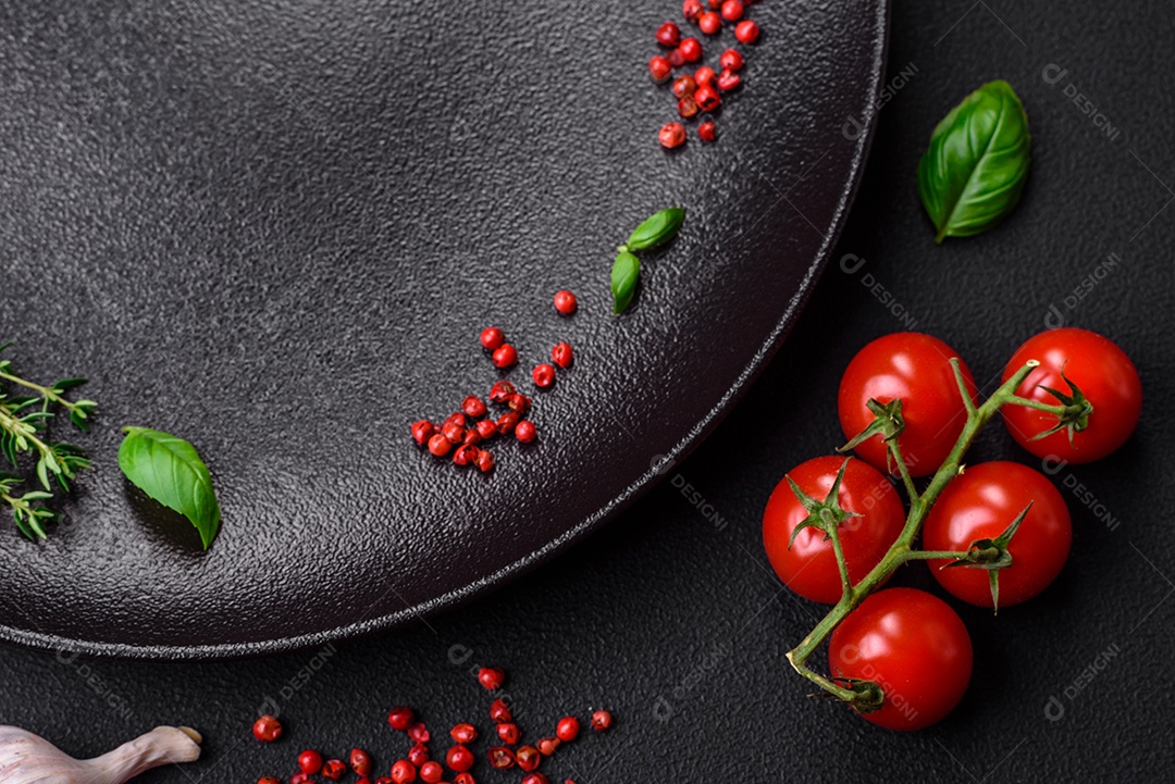 Ingredientes para cozinhar tomate cereja, sal, especiarias e ervas sobre um fundo escuro de concreto