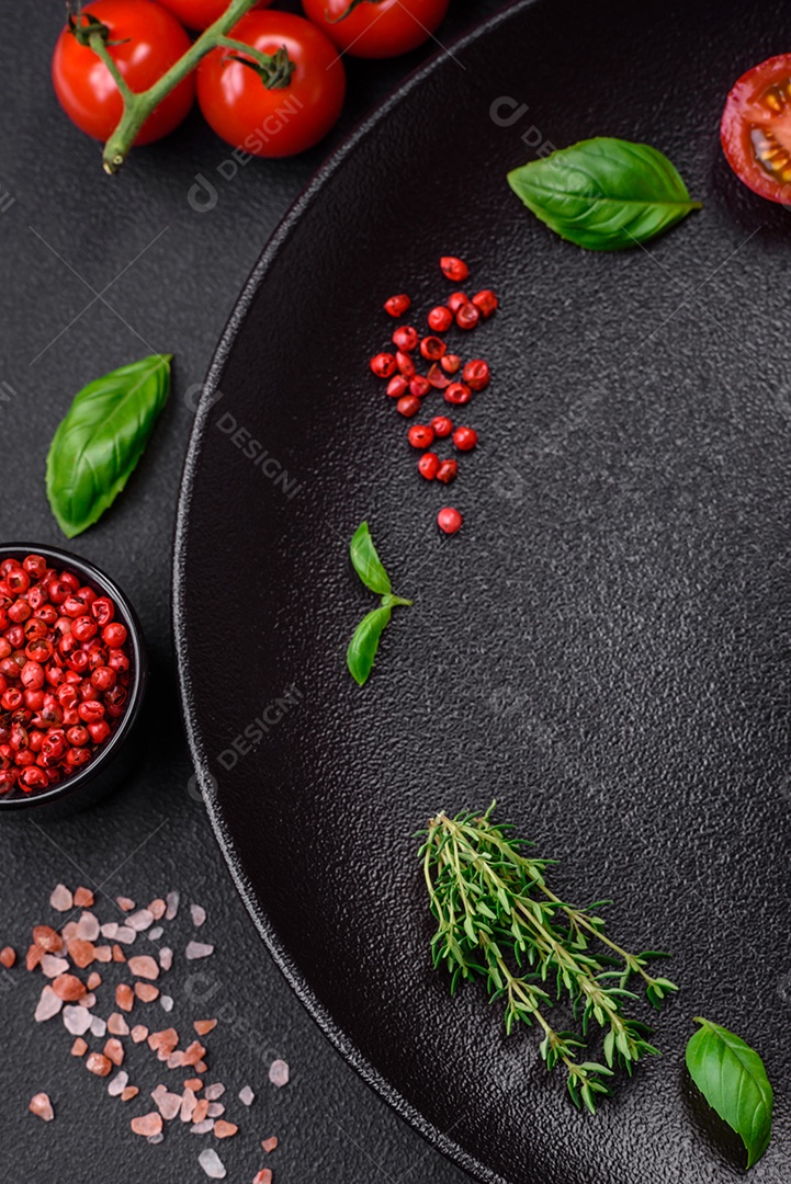 Ingredientes para cozinhar tomate cereja, sal, especiarias e ervas sobre um fundo escuro de concreto