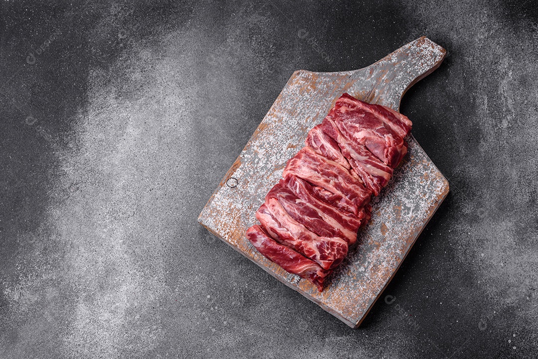 Costelas de carne crua fresca com sal, especiarias e ervas preparadas para grelhar