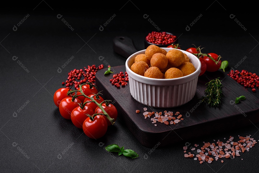 Deliciosas bolas de batata frita com mussarela à milanesa, sal, especiarias e ervas sobre um fundo escuro de concreto