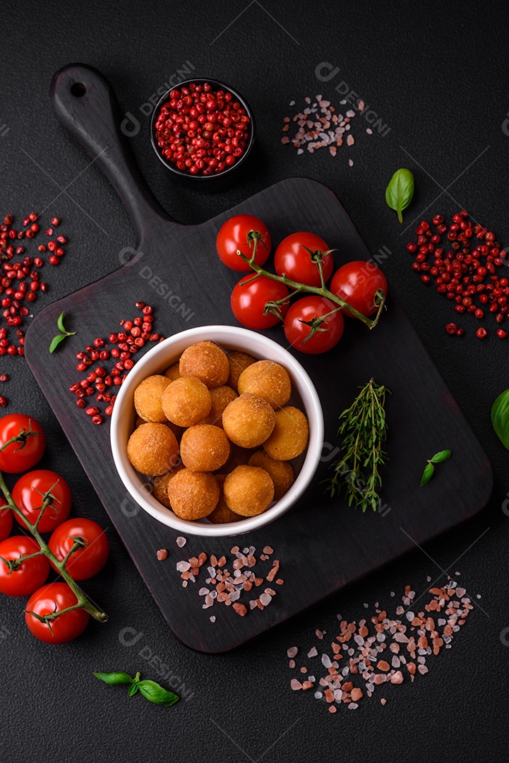 Deliciosas bolas de batata frita com mussarela à milanesa, sal, especiarias e ervas sobre um fundo escuro de concreto
