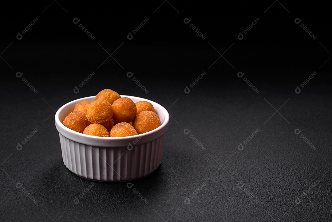 Deliciosas bolas de batata frita com mussarela à milanesa, sal, especiarias e ervas sobre um fundo escuro de concreto