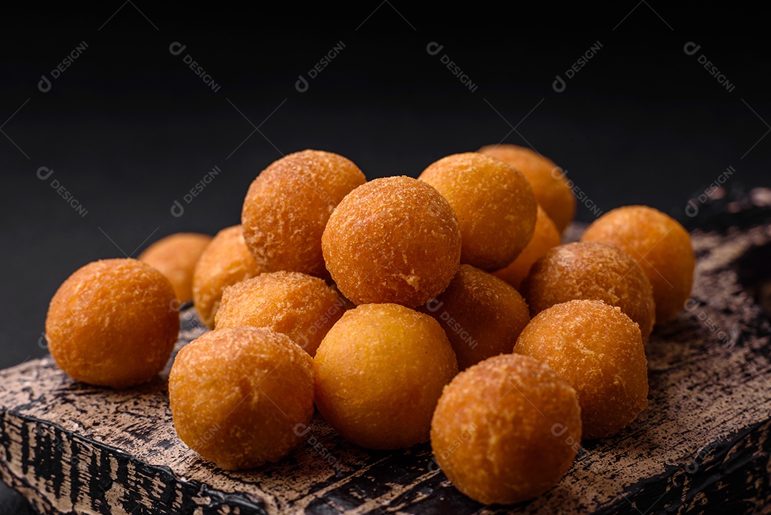 Deliciosas bolas de batata frita com mussarela à milanesa, sal, especiarias e ervas sobre um fundo escuro de concreto