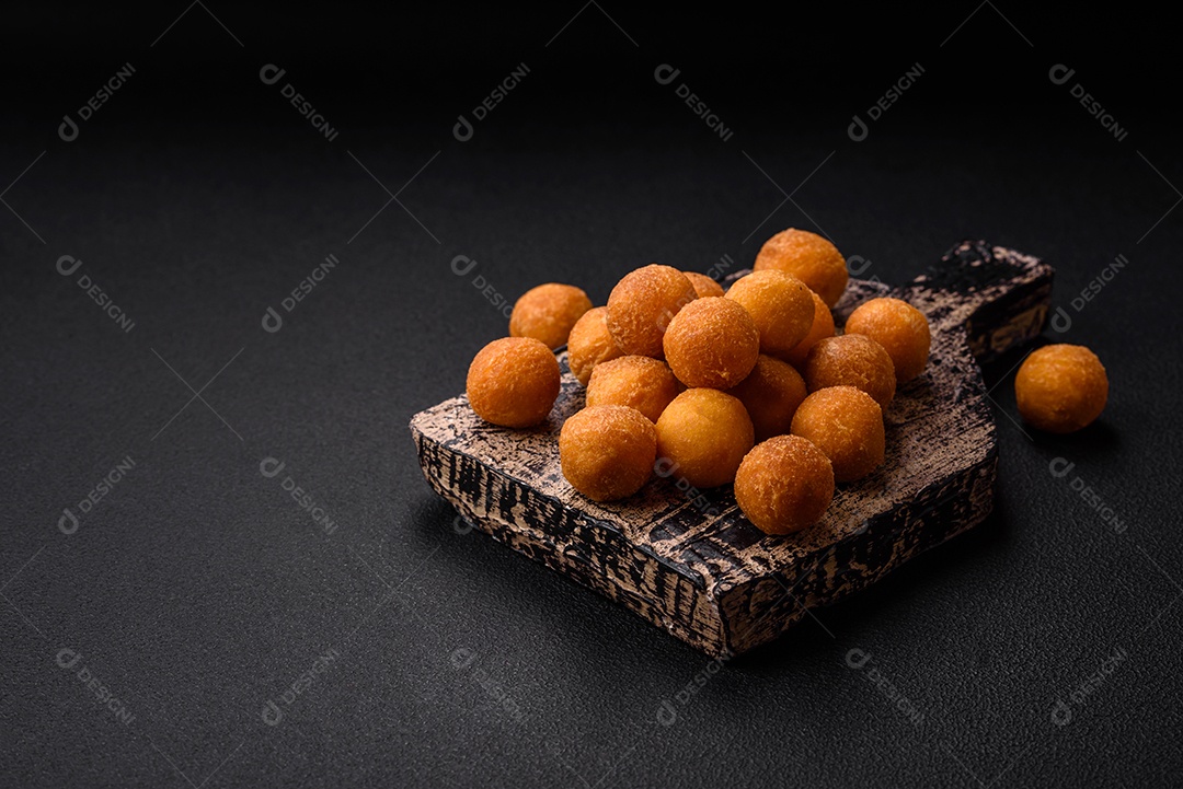 Deliciosas bolas de batata frita com mussarela à milanesa, sal, especiarias e ervas sobre um fundo escuro de concreto