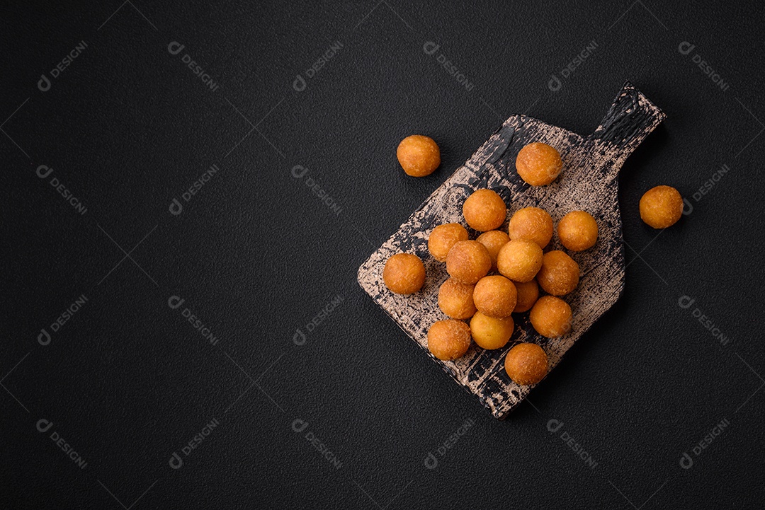 Deliciosas bolas de batata frita com mussarela à milanesa, sal, especiarias e ervas sobre um fundo escuro de concreto