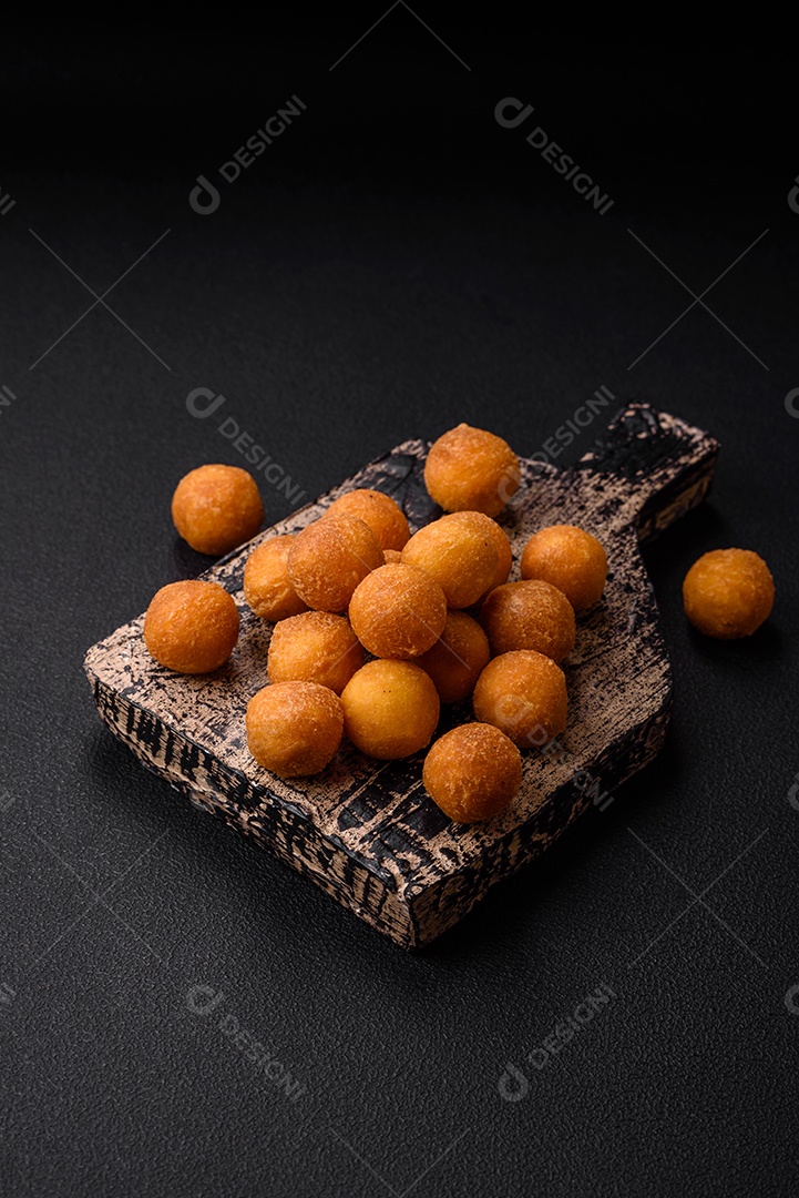 Deliciosas bolas de batata frita com mussarela à milanesa, sal, especiarias e ervas sobre um fundo escuro de concreto