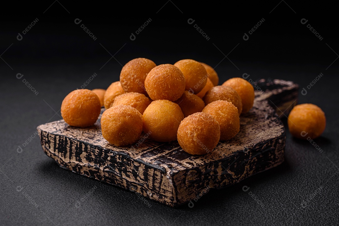 Deliciosas bolas de batata frita com mussarela à milanesa, sal, especiarias e ervas sobre um fundo escuro de concreto