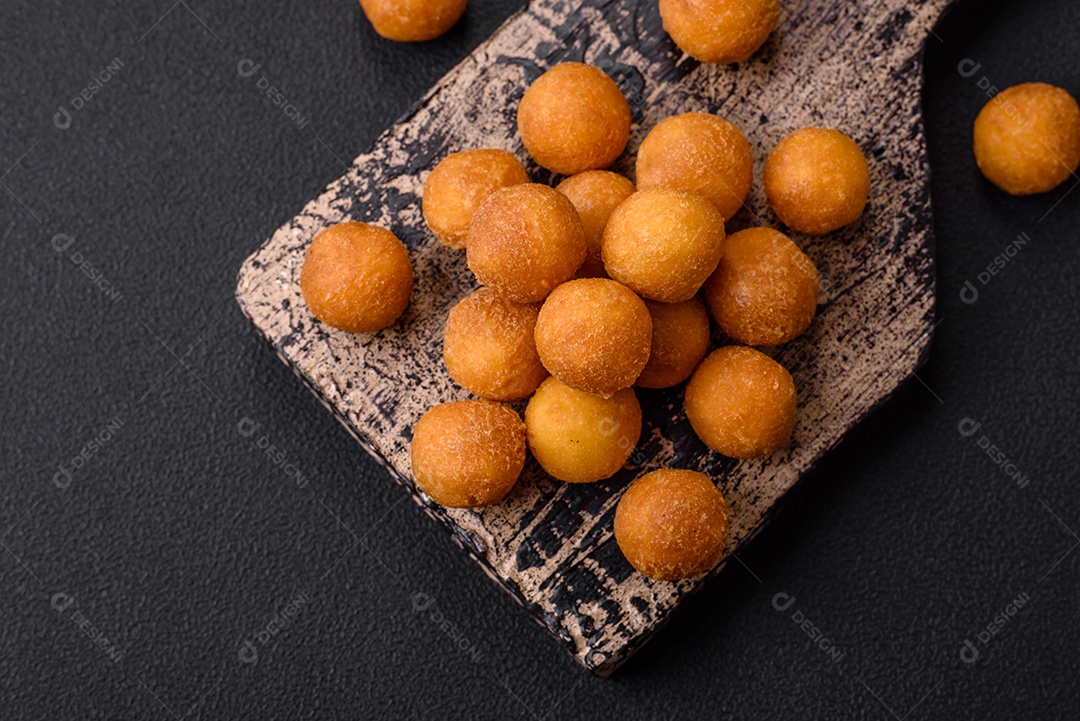 Deliciosas bolas de batata frita com mussarela à milanesa, sal, especiarias e ervas sobre um fundo escuro de concreto
