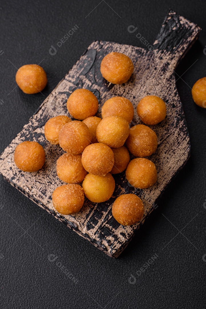 Deliciosas bolas de batata frita com mussarela à milanesa, sal, especiarias e ervas sobre um fundo escuro de concreto