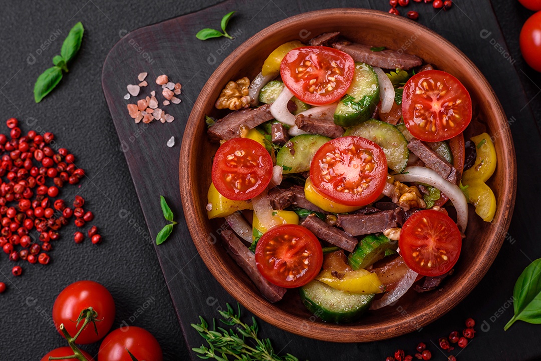 Deliciosa salada fresca com fatias de carne, tomate cereja, pimentão, sal, especiarias e ervas sobre um fundo de concreto texturizado