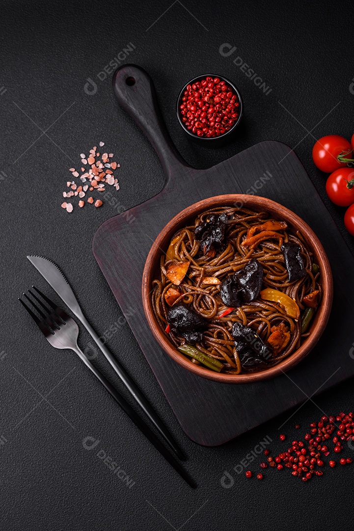 Delicioso macarrão de trigo sarraceno fresco ou udon com cogumelos, pimentões e outros vegetais, especiarias e ervas sobre um fundo escuro de concreto