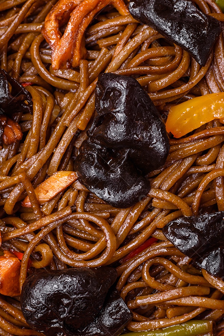 Delicioso macarrão de trigo sarraceno fresco ou udon com cogumelos, pimentões e outros vegetais, especiarias e ervas sobre um fundo escuro de concreto