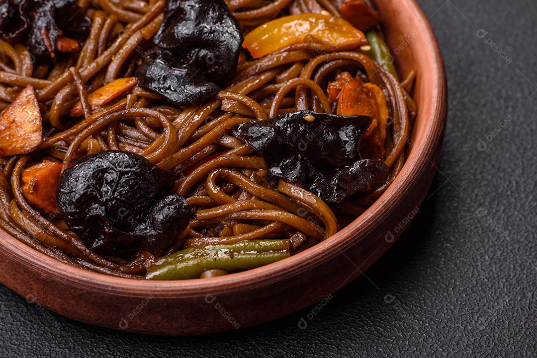 Delicioso macarrão de trigo sarraceno fresco ou udon com cogumelos, pimentões e outros vegetais, especiarias e ervas sobre um fundo escuro de concreto
