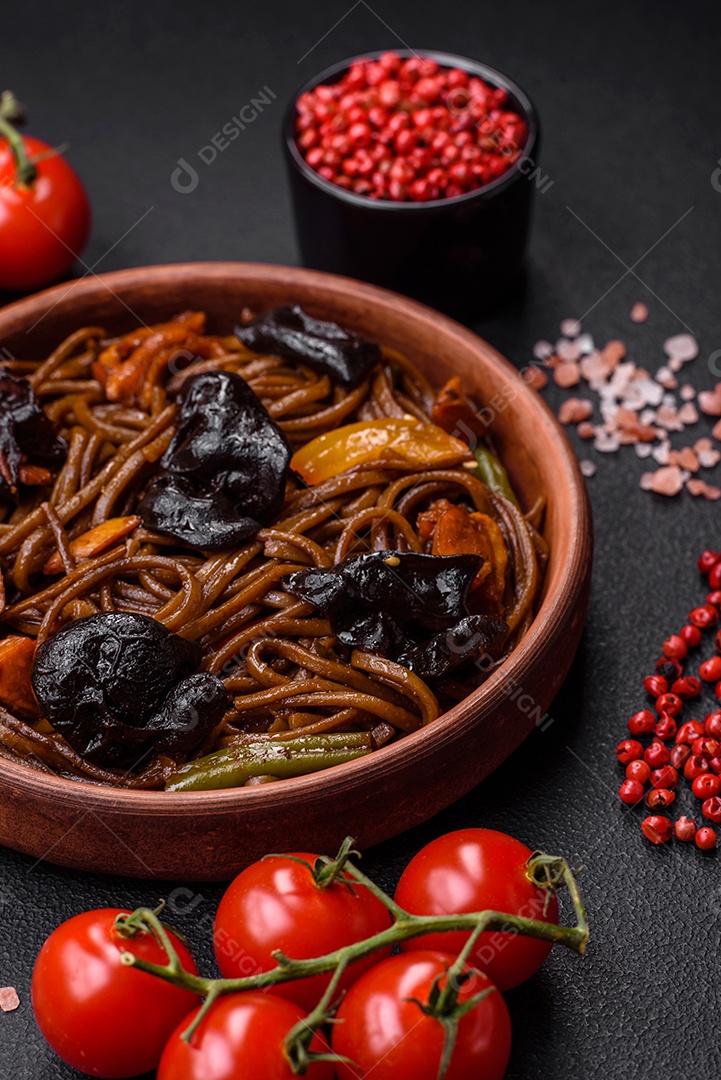 Delicioso macarrão de trigo sarraceno fresco ou udon com cogumelos, pimentões e outros vegetais, especiarias e ervas sobre um fundo escuro de concreto