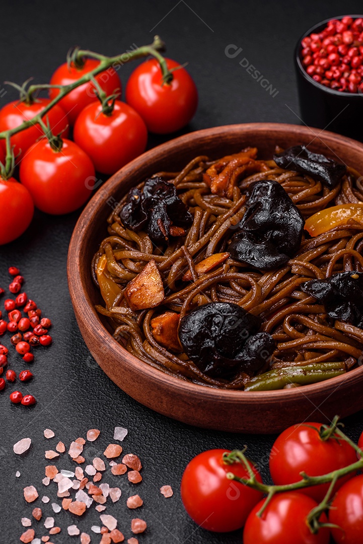 Delicioso macarrão de trigo sarraceno fresco ou udon com cogumelos, pimentões e outros vegetais, especiarias e ervas sobre um fundo escuro de concreto