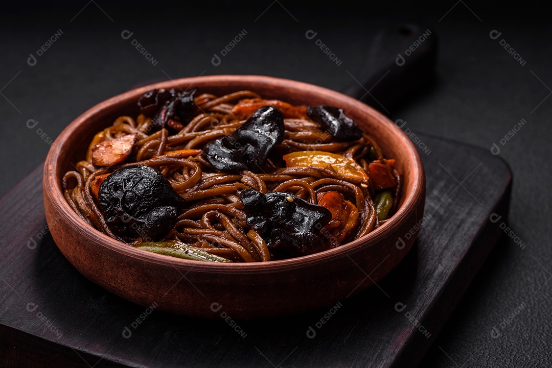 Delicioso macarrão de trigo sarraceno fresco ou udon com cogumelos, pimentões e outros vegetais, especiarias e ervas sobre um fundo escuro de concreto