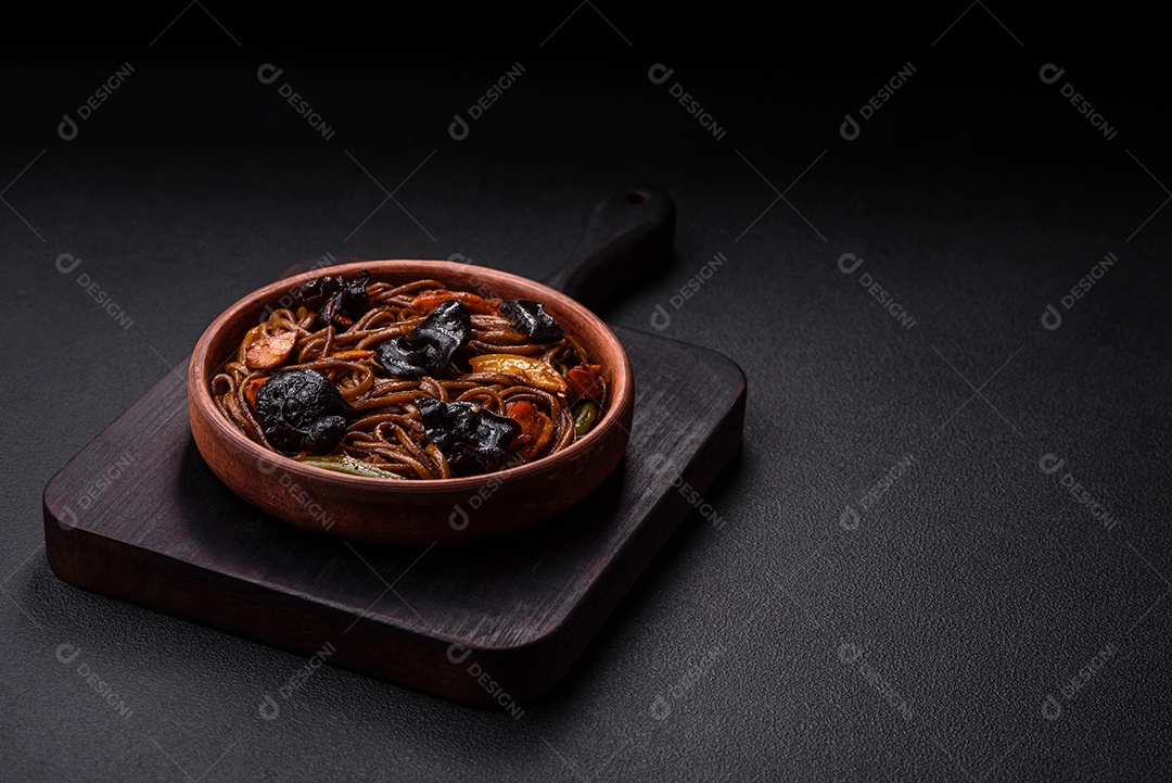 Delicioso macarrão de trigo sarraceno fresco ou udon com cogumelos, pimentões e outros vegetais, especiarias e ervas sobre um fundo escuro de concreto