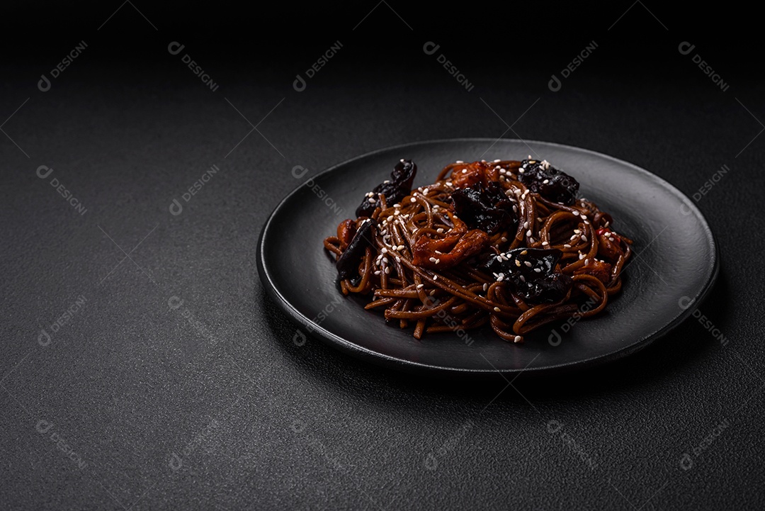 Delicioso macarrão de trigo sarraceno fresco ou udon com cogumelos, pimentões e outros vegetais, especiarias e ervas sobre um fundo escuro de concreto