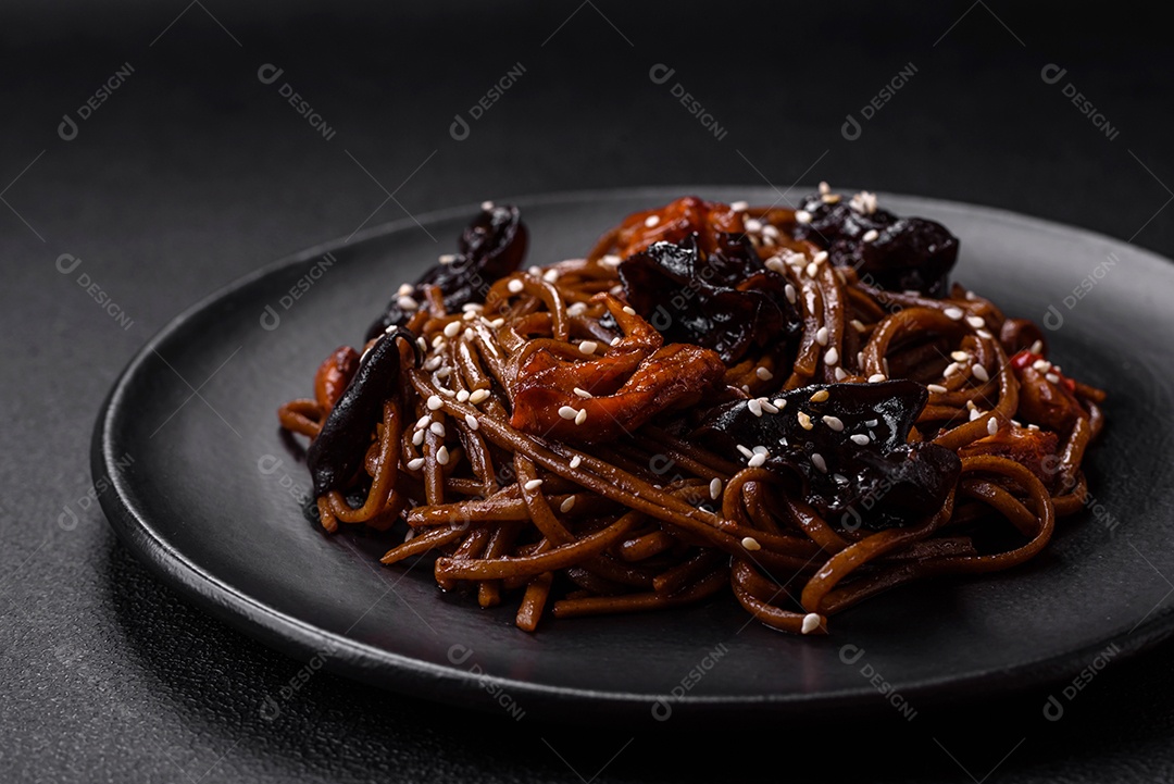 Delicioso macarrão de trigo sarraceno fresco ou udon com cogumelos, pimentões e outros vegetais, especiarias e ervas sobre um fundo escuro de concreto