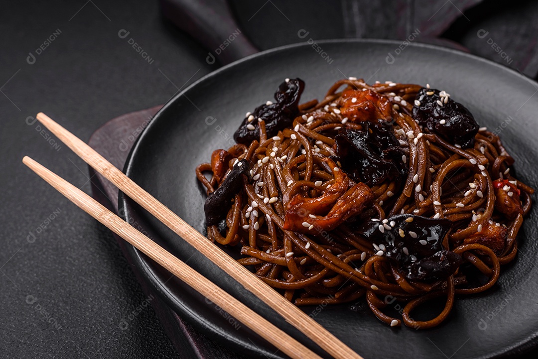 Delicioso macarrão de trigo sarraceno fresco ou udon com cogumelos, pimentões e outros vegetais, especiarias e ervas sobre um fundo escuro de concreto