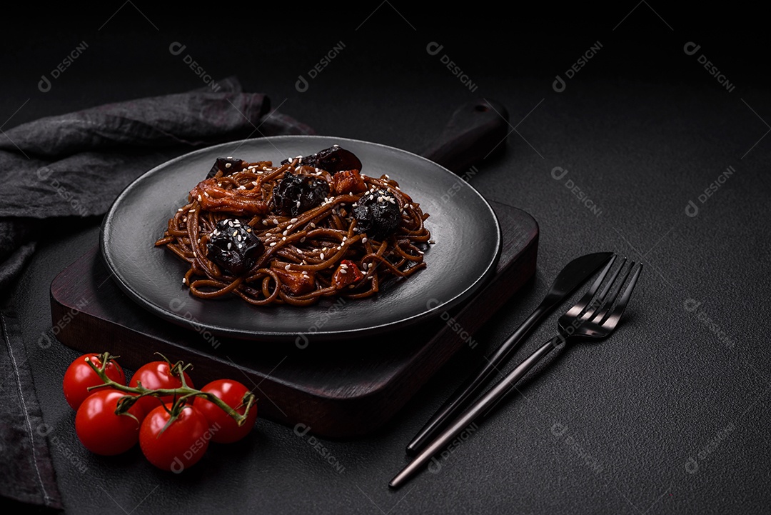 Delicioso macarrão de trigo sarraceno fresco ou udon com cogumelos, pimentões e outros vegetais, especiarias e ervas sobre um fundo escuro de concreto
