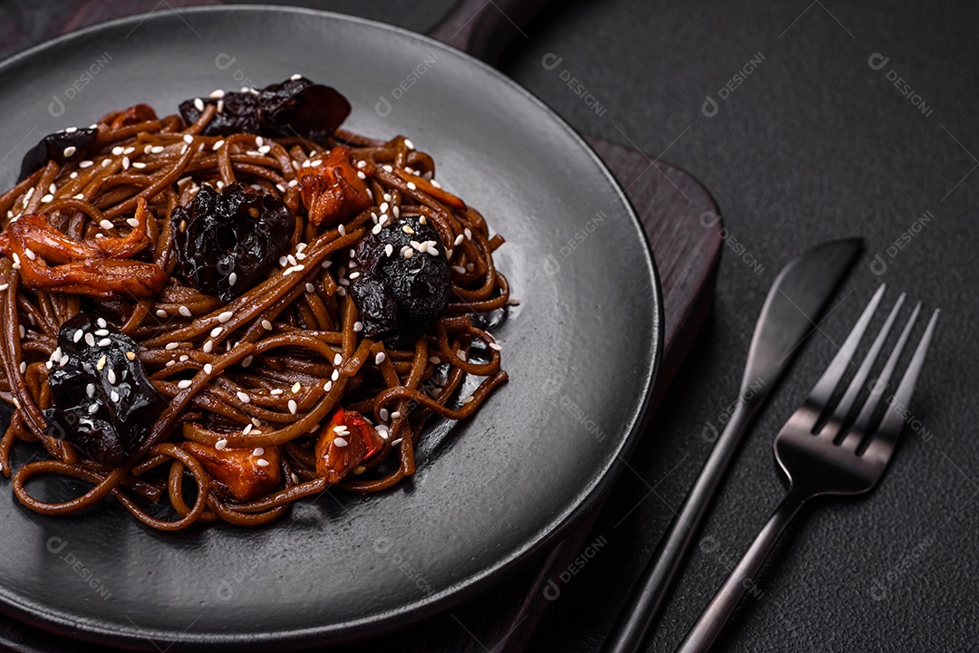 Delicioso macarrão de trigo sarraceno fresco ou udon com cogumelos, pimentões e outros vegetais, especiarias e ervas sobre um fundo escuro de concreto