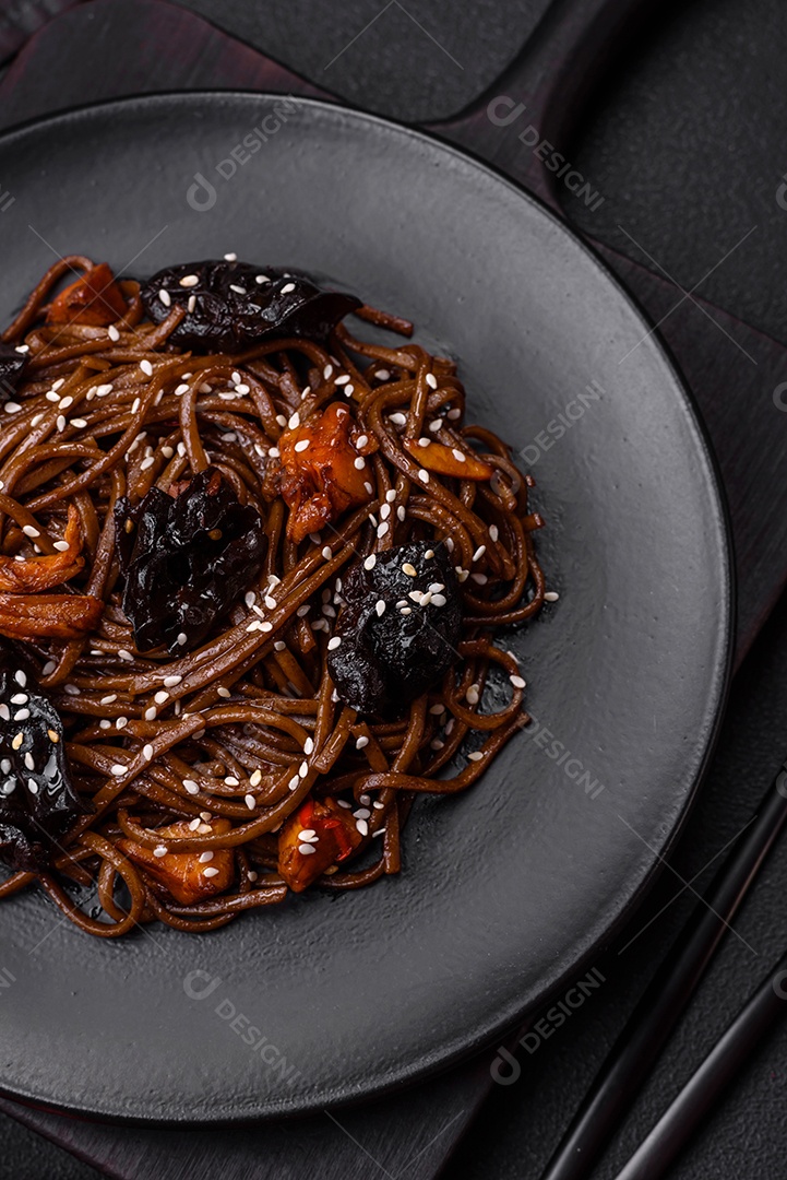 Delicioso macarrão de trigo sarraceno fresco ou udon com cogumelos, pimentões e outros vegetais, especiarias e ervas sobre um fundo escuro de concreto