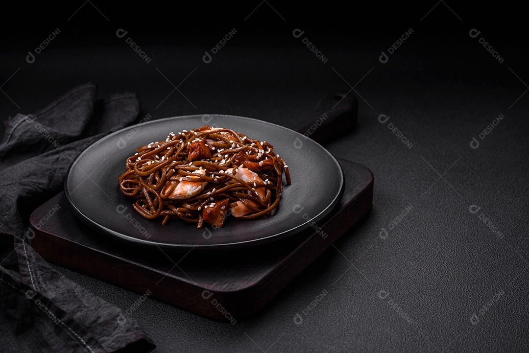 Delicioso macarrão de trigo sarraceno fresco ou udon com cogumelos, pimentões e outros vegetais, especiarias e ervas sobre um fundo escuro de concreto