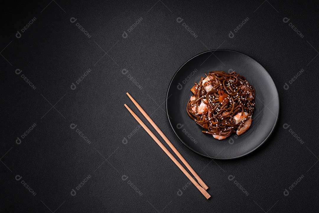 Delicioso macarrão de trigo sarraceno fresco ou udon com cogumelos, pimentões e outros vegetais, especiarias e ervas sobre um fundo escuro de concreto