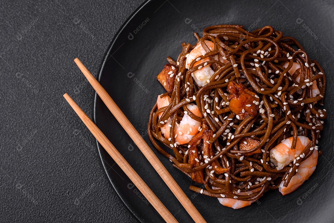 Delicioso macarrão de trigo sarraceno fresco ou udon com cogumelos, pimentões e outros vegetais, especiarias e ervas sobre um fundo escuro de concreto