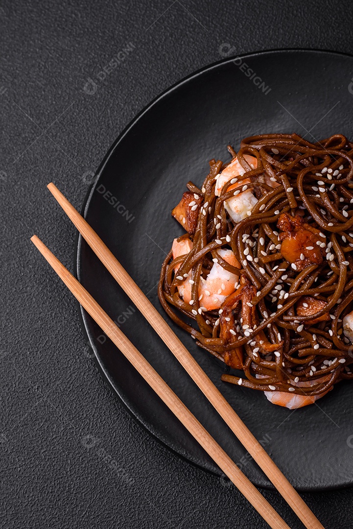 Delicioso macarrão de trigo sarraceno fresco ou udon com cogumelos, pimentões e outros vegetais, especiarias e ervas sobre um fundo escuro de concreto