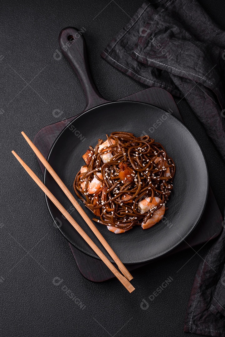 Delicioso macarrão de trigo sarraceno fresco ou udon com cogumelos, pimentões e outros vegetais, especiarias e ervas sobre um fundo escuro de concreto