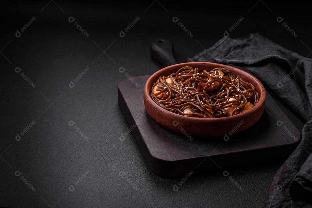 Delicioso macarrão de trigo sarraceno fresco ou udon com cogumelos, pimentões e outros vegetais, especiarias e ervas sobre um fundo escuro de concreto