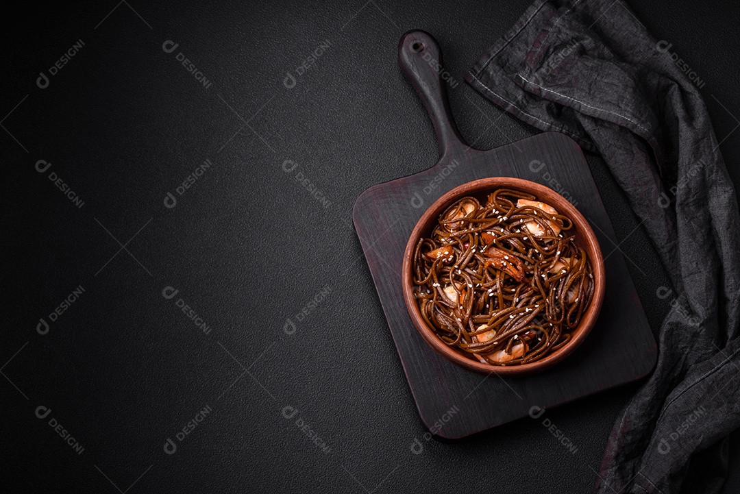 Delicioso macarrão de trigo sarraceno fresco ou udon com cogumelos, pimentões e outros vegetais, especiarias e ervas sobre um fundo escuro de concreto