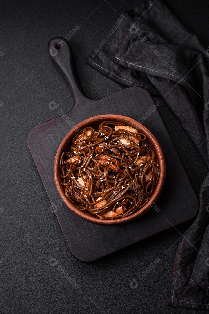 Delicioso macarrão de trigo sarraceno fresco ou udon com cogumelos, pimentões e outros vegetais, especiarias e ervas sobre um fundo escuro de concreto