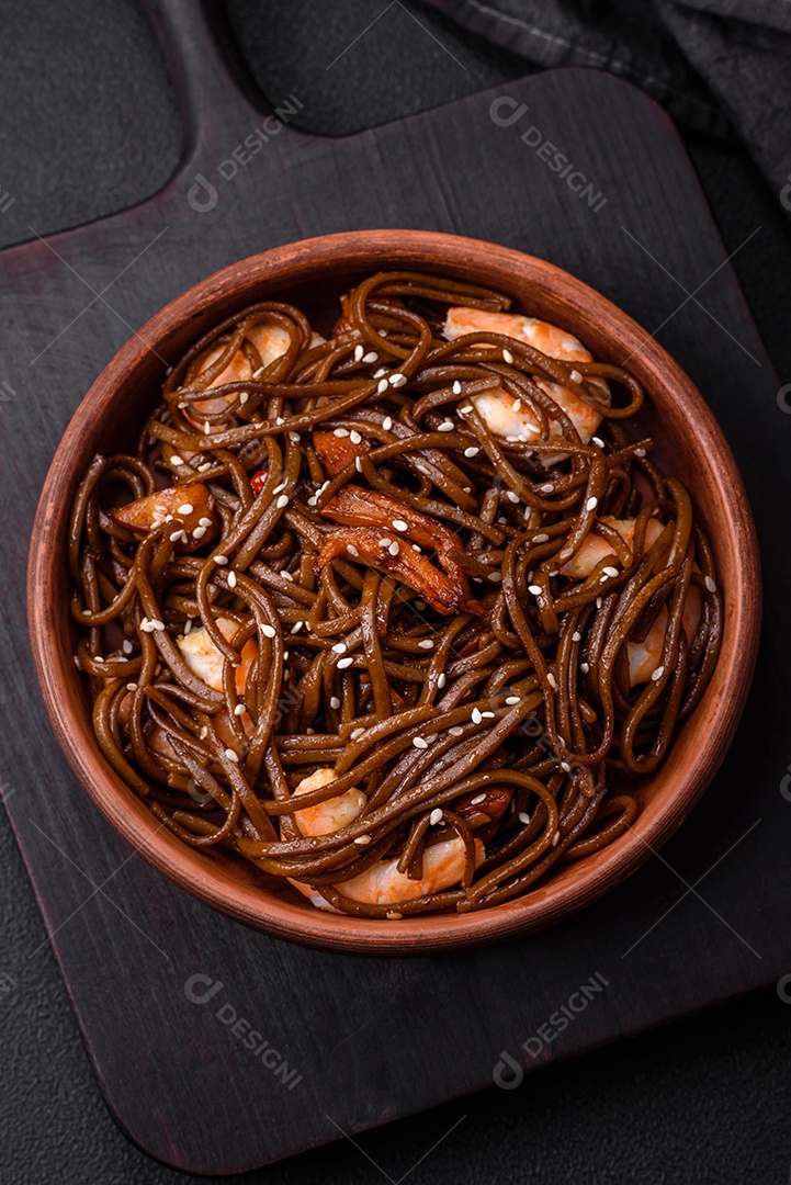 Delicioso macarrão de trigo sarraceno fresco ou udon com cogumelos, pimentões e outros vegetais, especiarias e ervas sobre um fundo escuro de concreto