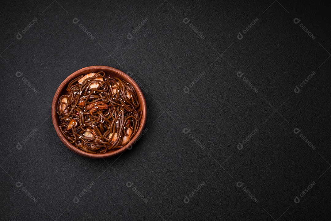 Delicioso macarrão de trigo sarraceno fresco ou udon com cogumelos, pimentões e outros vegetais, especiarias e ervas sobre um fundo escuro de concreto