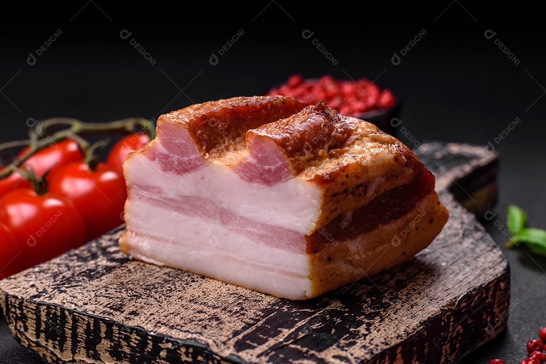 Delicioso bacon defumado com sal, especiarias e ervas sobre um fundo escuro de concreto